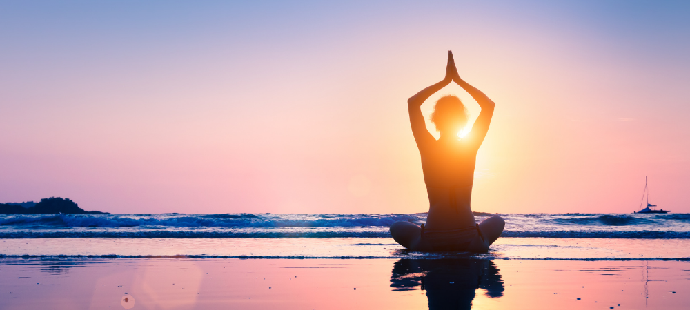 A woman in lotus pose on the beach at sunset