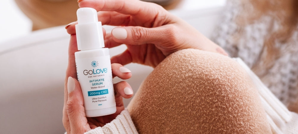 A woman holding a bottle of GoLove CBD serum on a sofa
