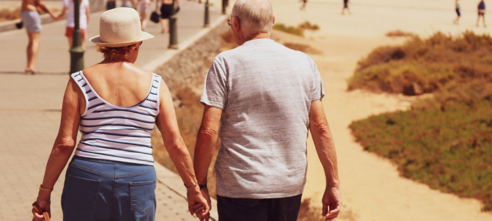 An older couple walking by beach holding hands