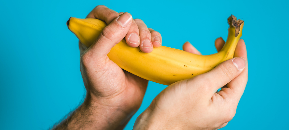 A pair of hands cupping and holding a banana suggestively 