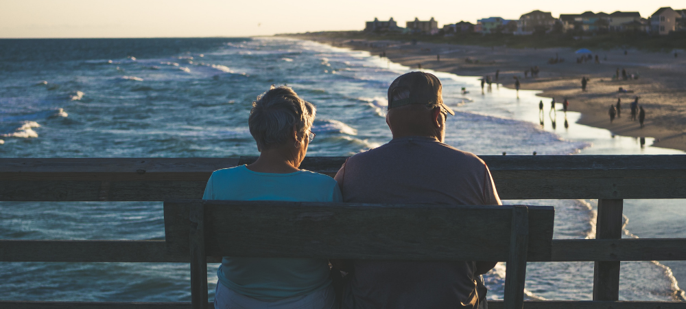 An older couple sitting on a bench looking at the ocean